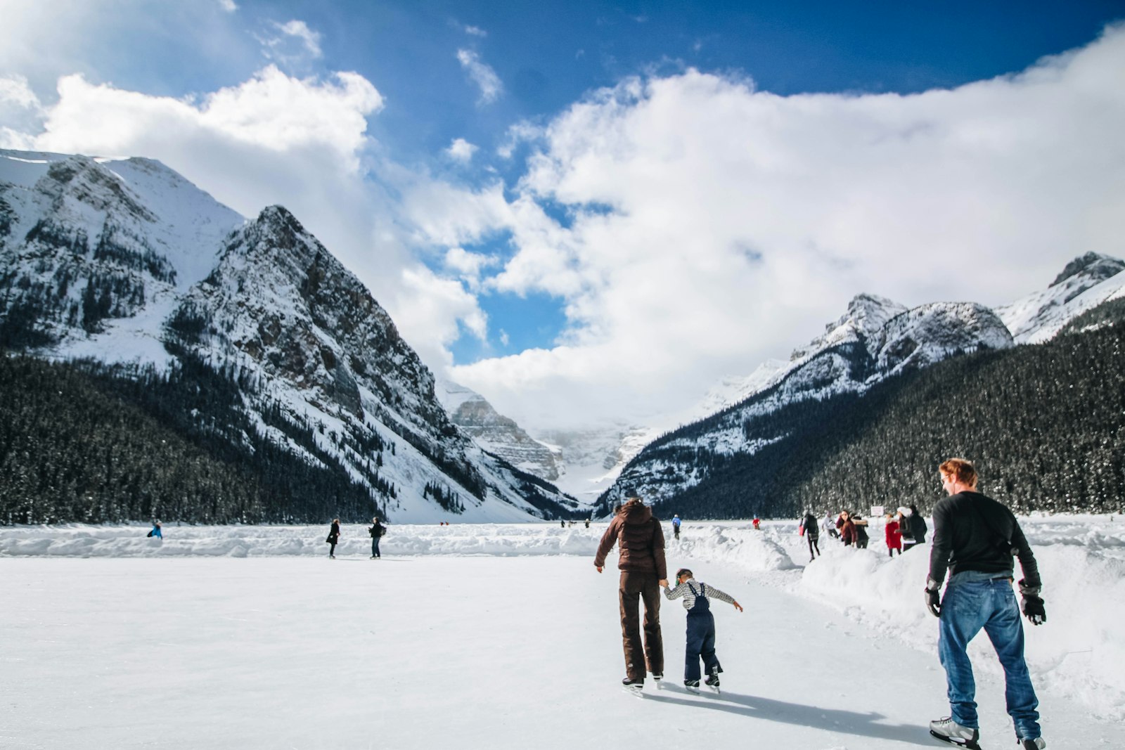 Skaters on a frozen lake surrounded by snowy mountains in the Canadian Rockies